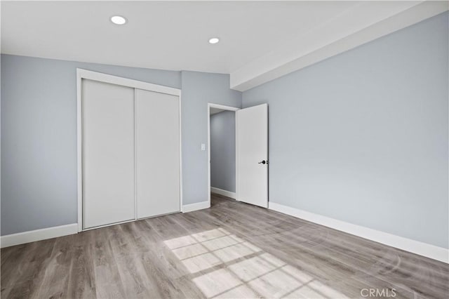 unfurnished bedroom featuring vaulted ceiling, a closet, and light hardwood / wood-style floors