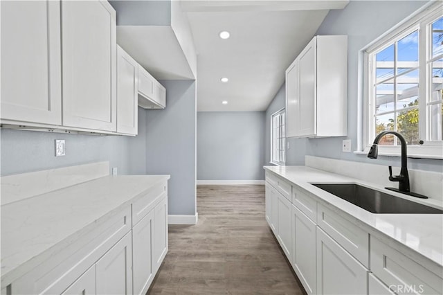 kitchen featuring hardwood / wood-style flooring, sink, white cabinets, and light stone countertops