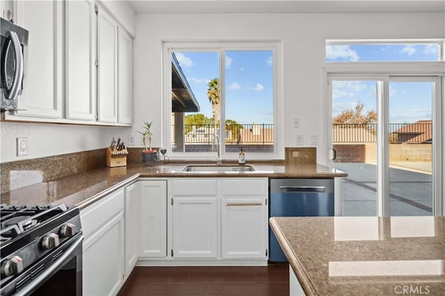 kitchen with appliances with stainless steel finishes, white cabinetry, dark stone counters, and sink