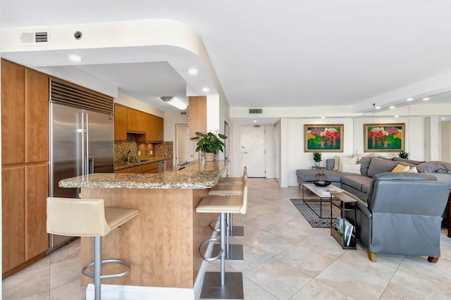 kitchen featuring brown cabinetry, a peninsula, a sink, a kitchen bar, and open floor plan