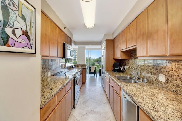 kitchen featuring light stone counters, light tile patterned flooring, a sink, appliances with stainless steel finishes, and tasteful backsplash