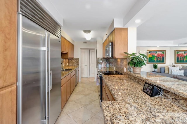 kitchen featuring decorative backsplash, light stone countertops, appliances with stainless steel finishes, and a sink