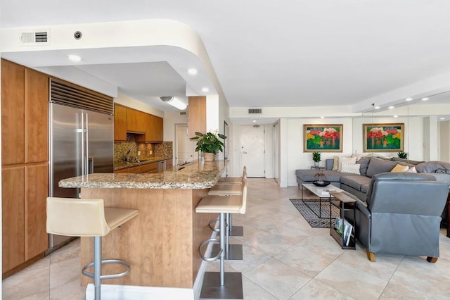 kitchen with a sink, a breakfast bar area, a peninsula, open floor plan, and brown cabinetry