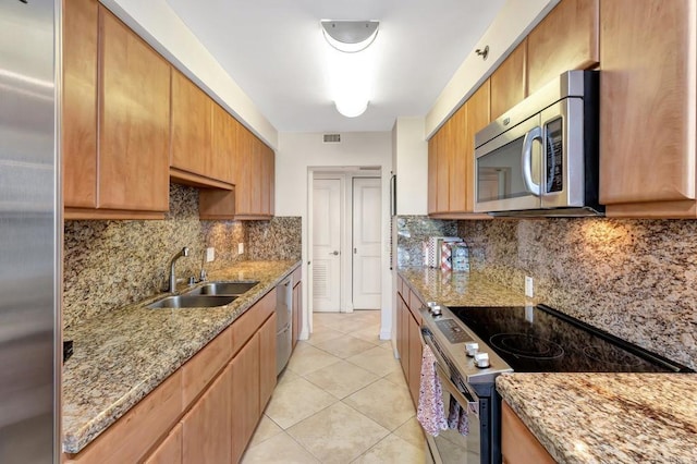 kitchen featuring light stone countertops, appliances with stainless steel finishes, a sink, backsplash, and light tile patterned floors