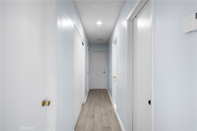 hallway with a textured ceiling and light hardwood / wood-style flooring