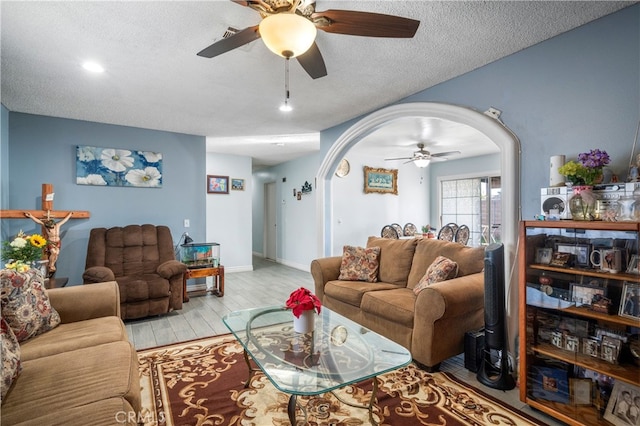 living room featuring light wood-type flooring, ceiling fan, and a textured ceiling