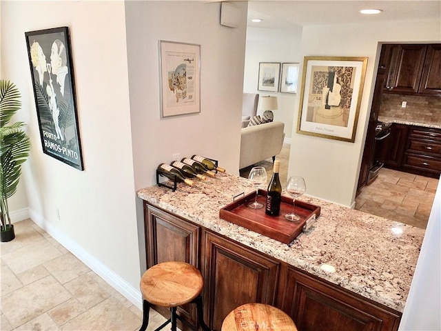 bar with decorative backsplash, dark brown cabinets, and light stone counters