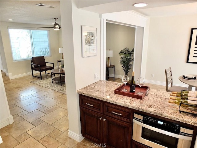 kitchen featuring ceiling fan, light stone countertops, and dark brown cabinets