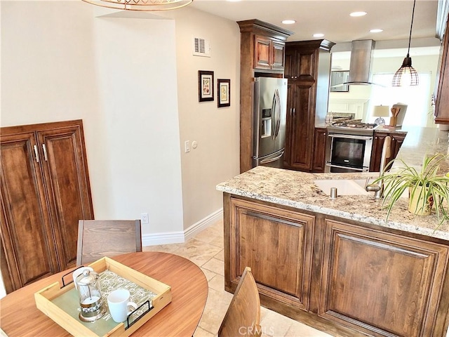 kitchen featuring light stone countertops, pendant lighting, wall chimney range hood, stainless steel appliances, and light tile patterned floors