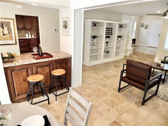 bar with ceiling fan, light stone counters, and tasteful backsplash