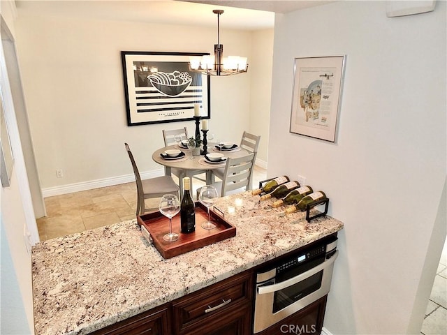 kitchen featuring a chandelier, dark brown cabinets, light stone counters, and decorative light fixtures