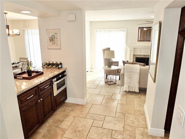 kitchen featuring ceiling fan with notable chandelier, light stone countertops, decorative light fixtures, a fireplace, and oven