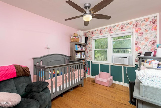 bedroom with ceiling fan, a nursery area, cooling unit, and light hardwood / wood-style flooring