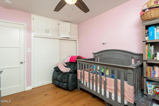 bedroom featuring light wood-type flooring, ceiling fan, a closet, and a crib