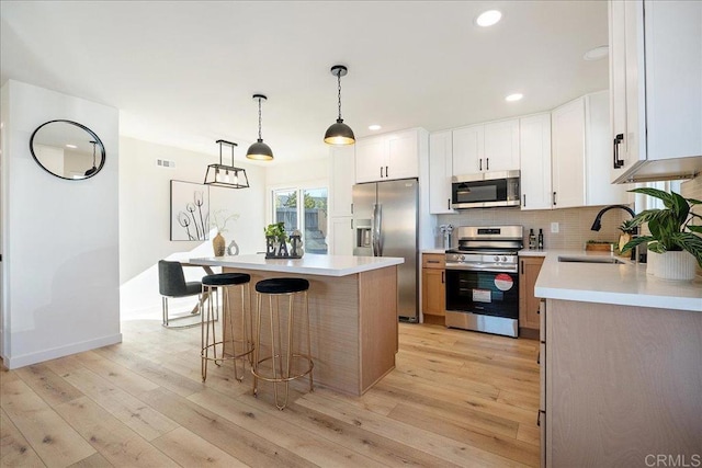 kitchen with decorative light fixtures, a kitchen island, sink, white cabinetry, and appliances with stainless steel finishes