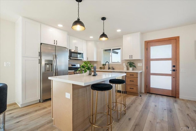 kitchen featuring stainless steel appliances, white cabinetry, a kitchen island, and hanging light fixtures