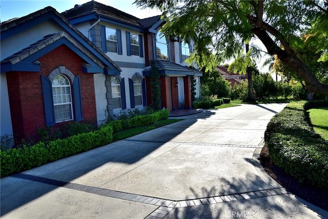 view of property exterior with concrete driveway, brick siding, a tiled roof, and stucco siding