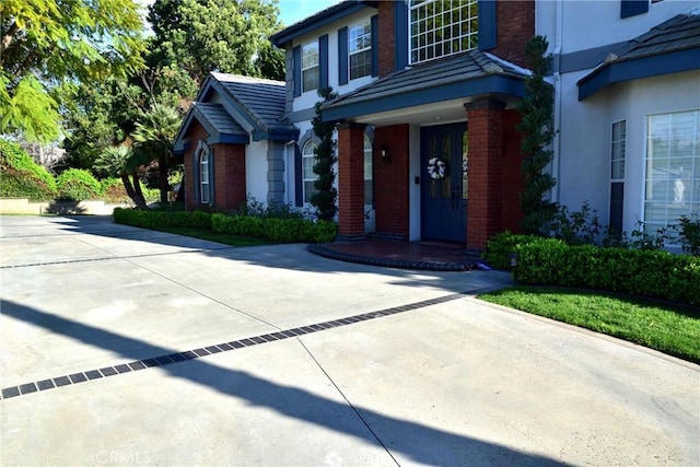 property entrance with driveway, brick siding, a tile roof, and stucco siding