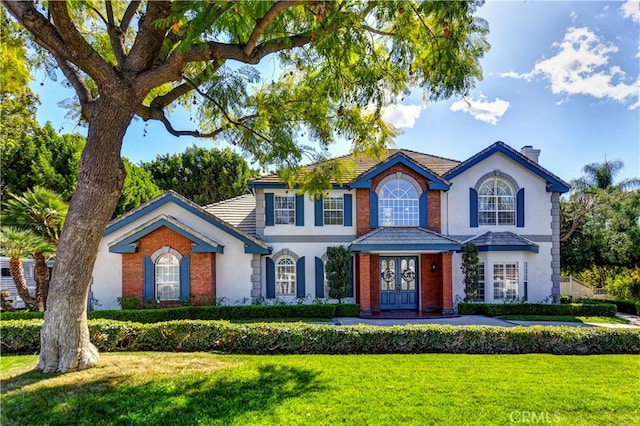 view of front of house featuring french doors, brick siding, a chimney, stucco siding, and a front lawn