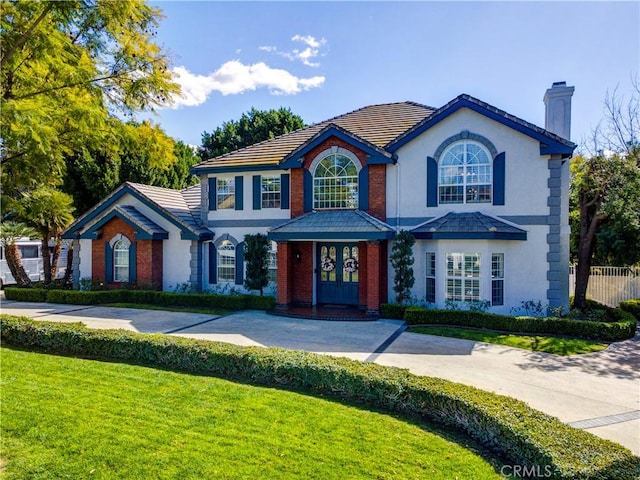 view of front of house featuring a tile roof, fence, stucco siding, a front lawn, and a chimney