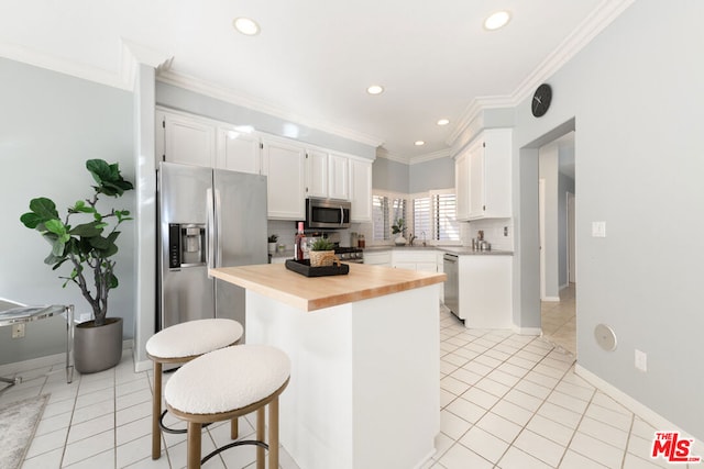 kitchen with wood counters, appliances with stainless steel finishes, white cabinetry, and a breakfast bar