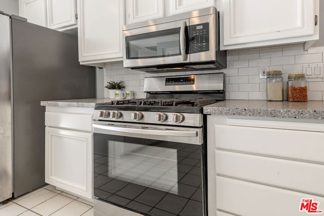 kitchen with light stone countertops, white cabinets, stainless steel appliances, backsplash, and light tile patterned flooring