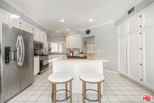 kitchen featuring appliances with stainless steel finishes, a kitchen bar, white cabinetry, decorative backsplash, and ornamental molding