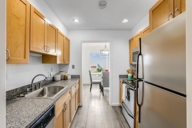 kitchen with stainless steel appliances, decorative light fixtures, light wood-type flooring, dark stone countertops, and sink