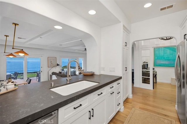 kitchen with appliances with stainless steel finishes, sink, white cabinets, a water view, and beam ceiling