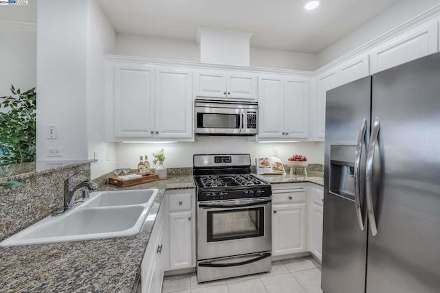 kitchen with light tile patterned floors, stainless steel appliances, dark stone counters, white cabinets, and sink