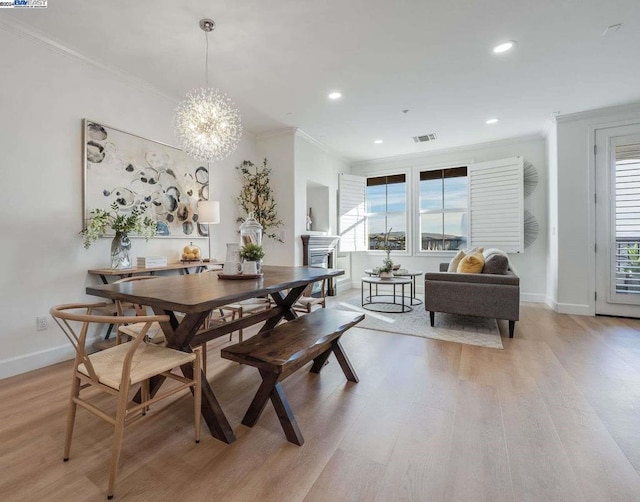 dining space featuring light wood-type flooring, ornamental molding, and an inviting chandelier