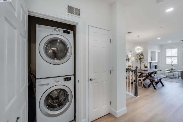 laundry area with stacked washing maching and dryer, light wood-type flooring, and an inviting chandelier