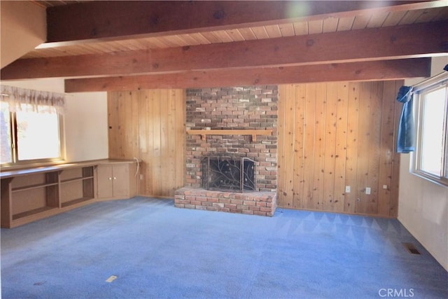 unfurnished living room with carpet, a brick fireplace, beamed ceiling, and wooden walls