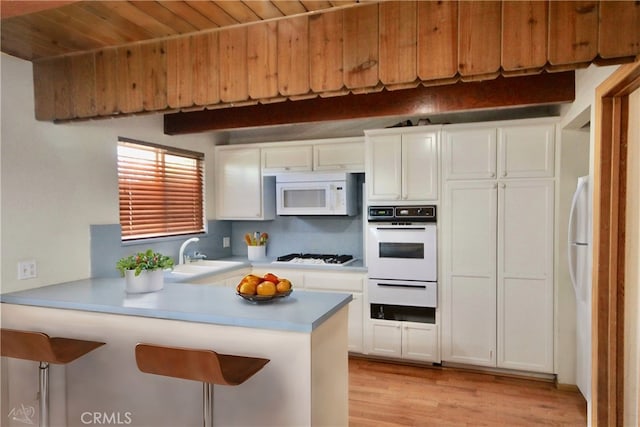 kitchen featuring white appliances, white cabinets, sink, kitchen peninsula, and a breakfast bar area