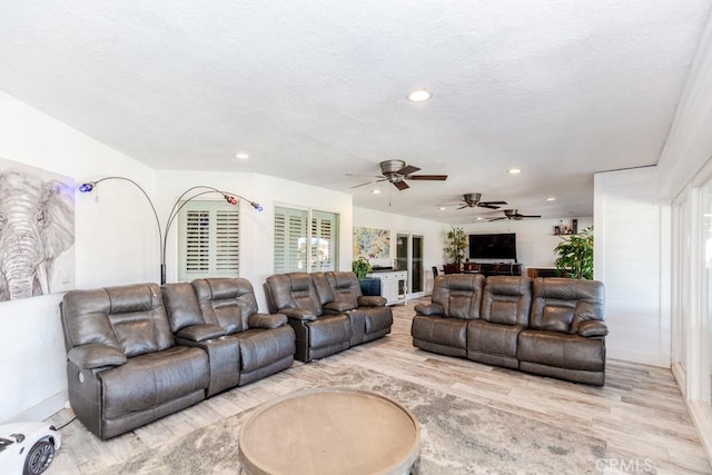 living room featuring ceiling fan, a textured ceiling, and light wood-type flooring