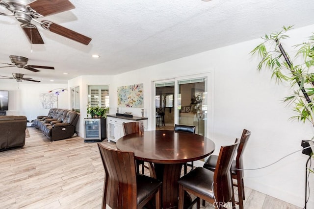 dining room with a textured ceiling, wine cooler, and light hardwood / wood-style flooring