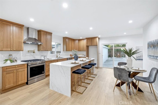 kitchen with wall chimney exhaust hood, gas stove, a kitchen island, a kitchen breakfast bar, and light hardwood / wood-style flooring