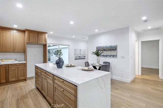 kitchen with light wood-type flooring, light stone counters, and a kitchen island