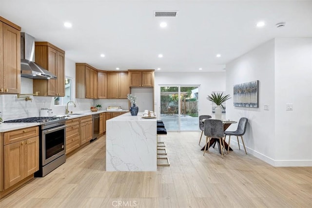 kitchen with tasteful backsplash, a kitchen island, light wood-type flooring, appliances with stainless steel finishes, and wall chimney exhaust hood