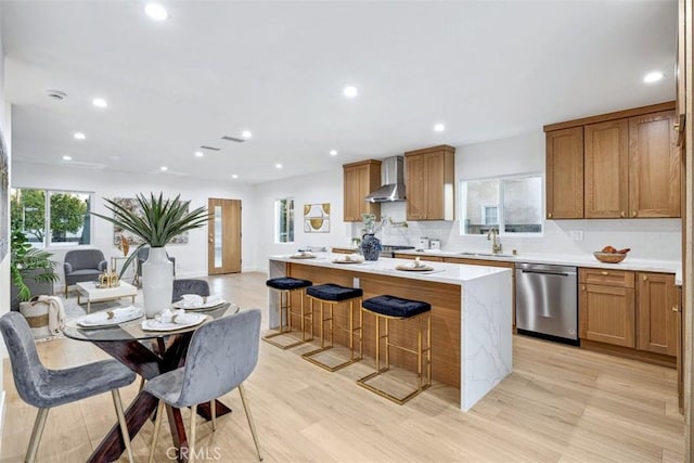 kitchen with a center island, stainless steel dishwasher, a kitchen bar, light wood-type flooring, and wall chimney exhaust hood