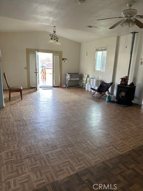 interior space featuring vaulted ceiling, dark parquet flooring, ceiling fan with notable chandelier, and a wood stove