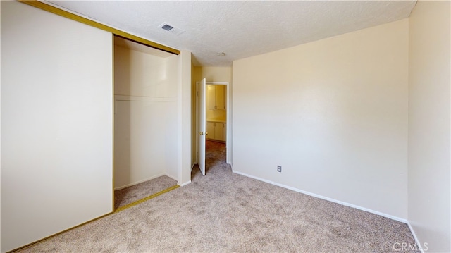 unfurnished bedroom featuring light carpet, a textured ceiling, and a closet