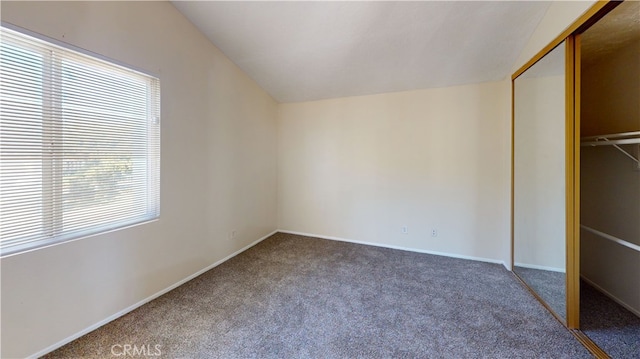 unfurnished bedroom featuring lofted ceiling, a closet, and carpet flooring