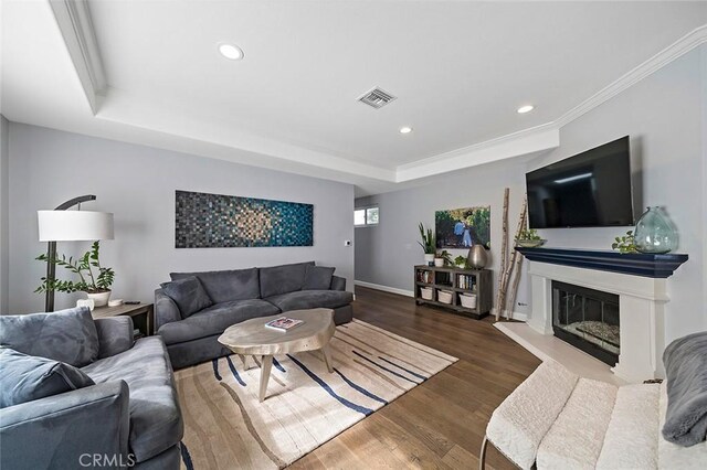 living room featuring hardwood / wood-style flooring, ornamental molding, and a raised ceiling