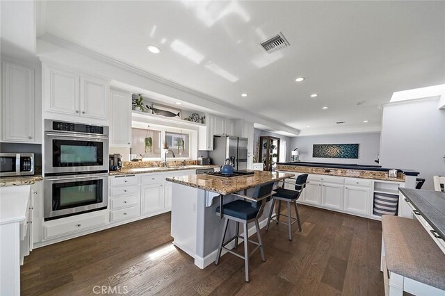 kitchen with a kitchen island, a kitchen bar, sink, stainless steel appliances, and white cabinets