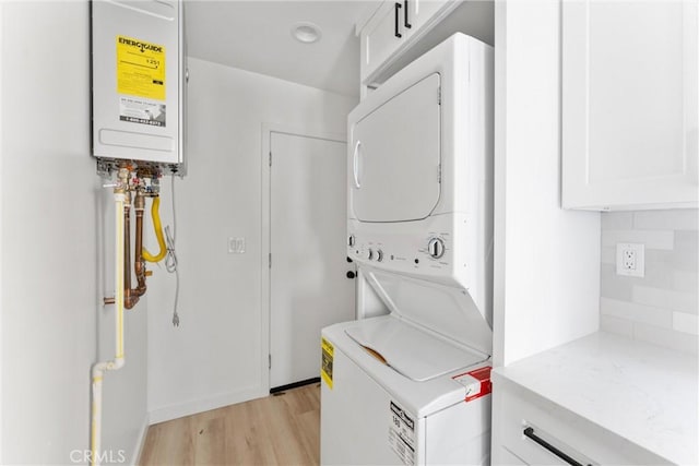 clothes washing area with water heater, cabinets, stacked washer and dryer, and light wood-type flooring