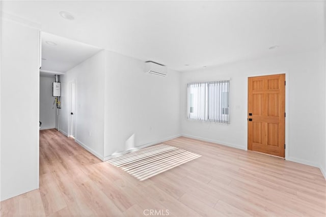 empty room with water heater, light wood-type flooring, and a wall mounted air conditioner