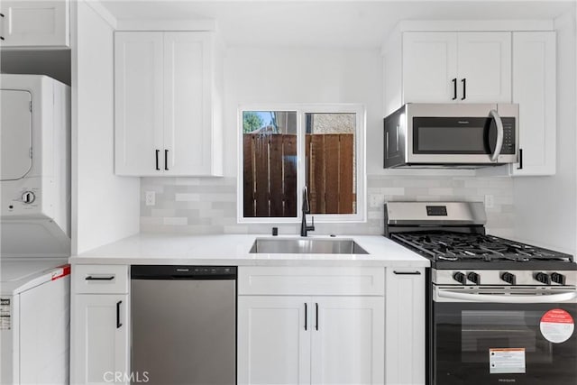 kitchen featuring backsplash, sink, appliances with stainless steel finishes, stacked washer and clothes dryer, and white cabinets