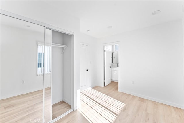 unfurnished bedroom featuring ensuite bath, a closet, and light hardwood / wood-style floors