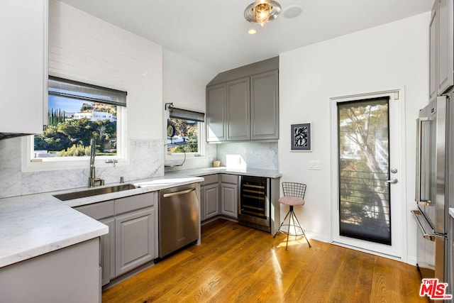 kitchen with beverage cooler, appliances with stainless steel finishes, sink, gray cabinets, and hardwood / wood-style flooring